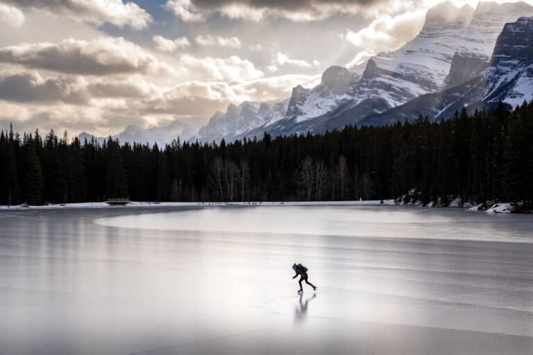 A person ice skating on a frozen mountain lake in Banff National Park